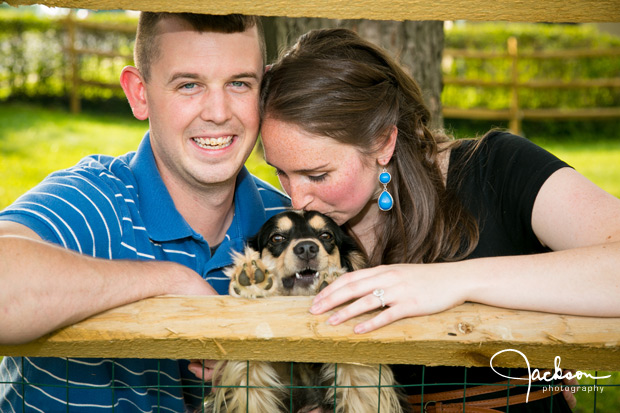 couple posing with puppy beneath fence