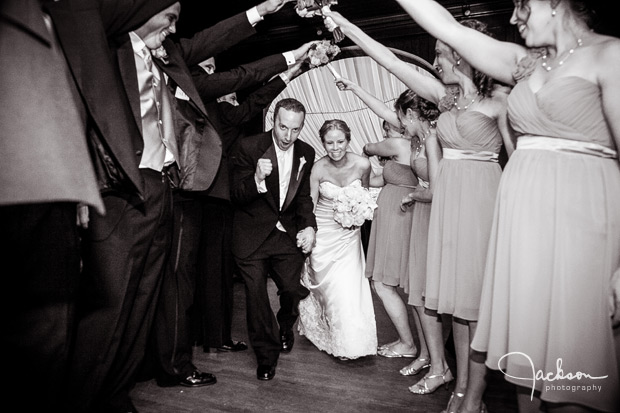 bride and groom entering reception beneath bridge of arms