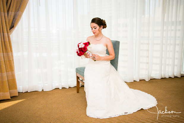 bride sitting in blue chair with red and white bouquet