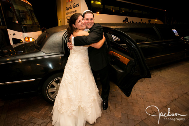 bride and groom hugging in front of limo