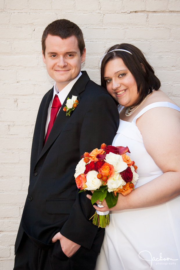 bride and groom by white brick wall