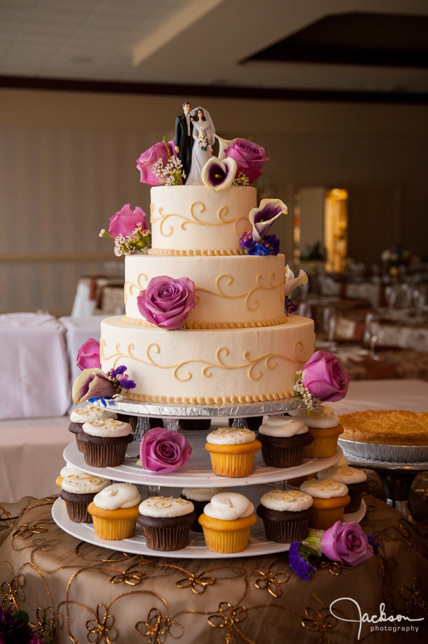 round white flowered wedding cake with cupcakes at the base